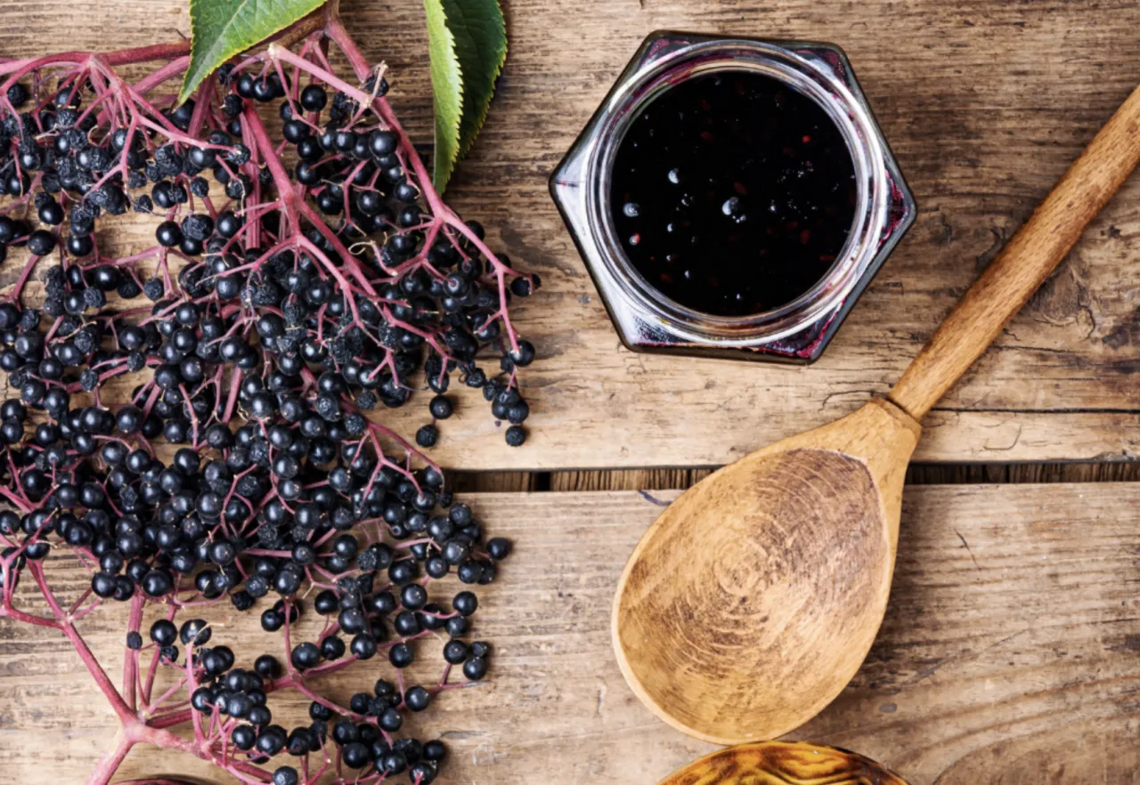 Looking down on a wood table of berries, a wooden spoon, and a container of jam.